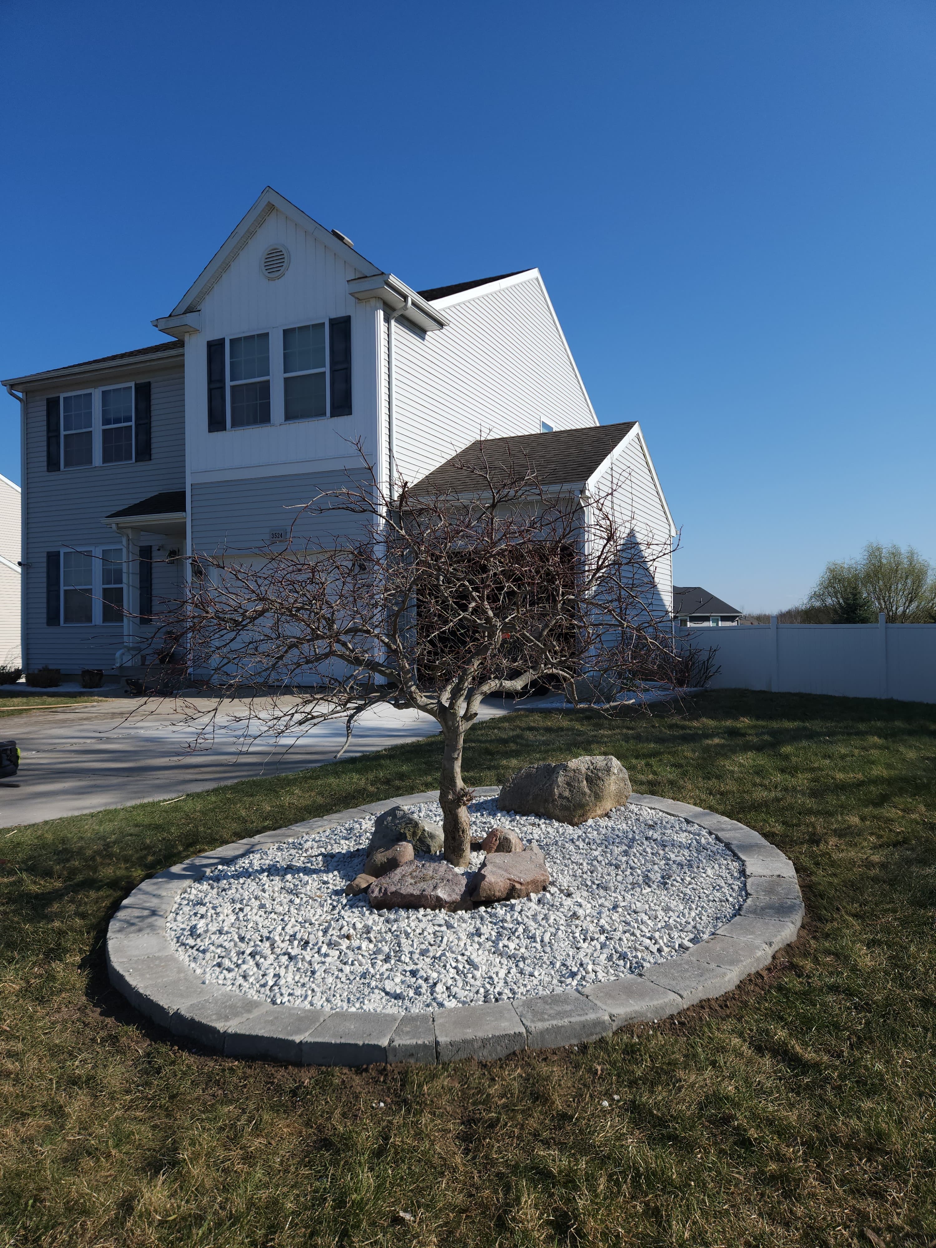 Circular paver-edged front-yard bed with white rock, ornamental tree, and boulder accent installed by Bernal Landscape