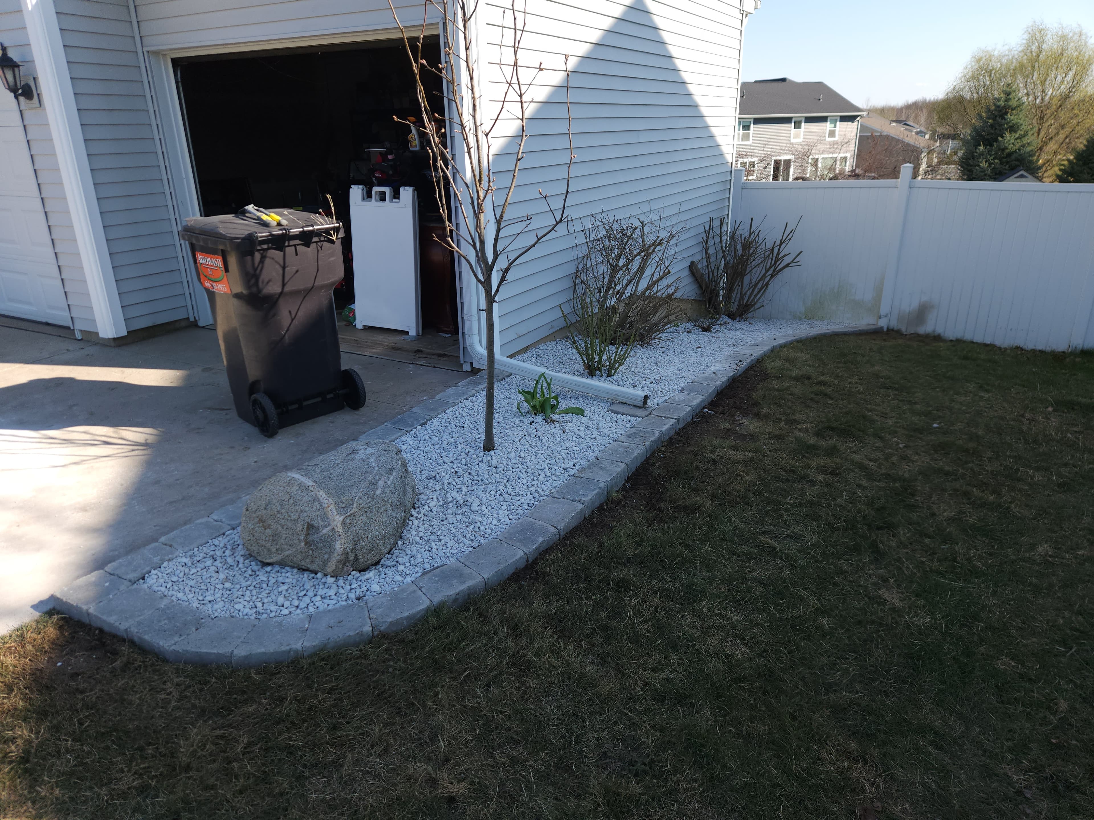 Curved paver-edged landscape bed with white rock and a decorative boulder along the side of a home