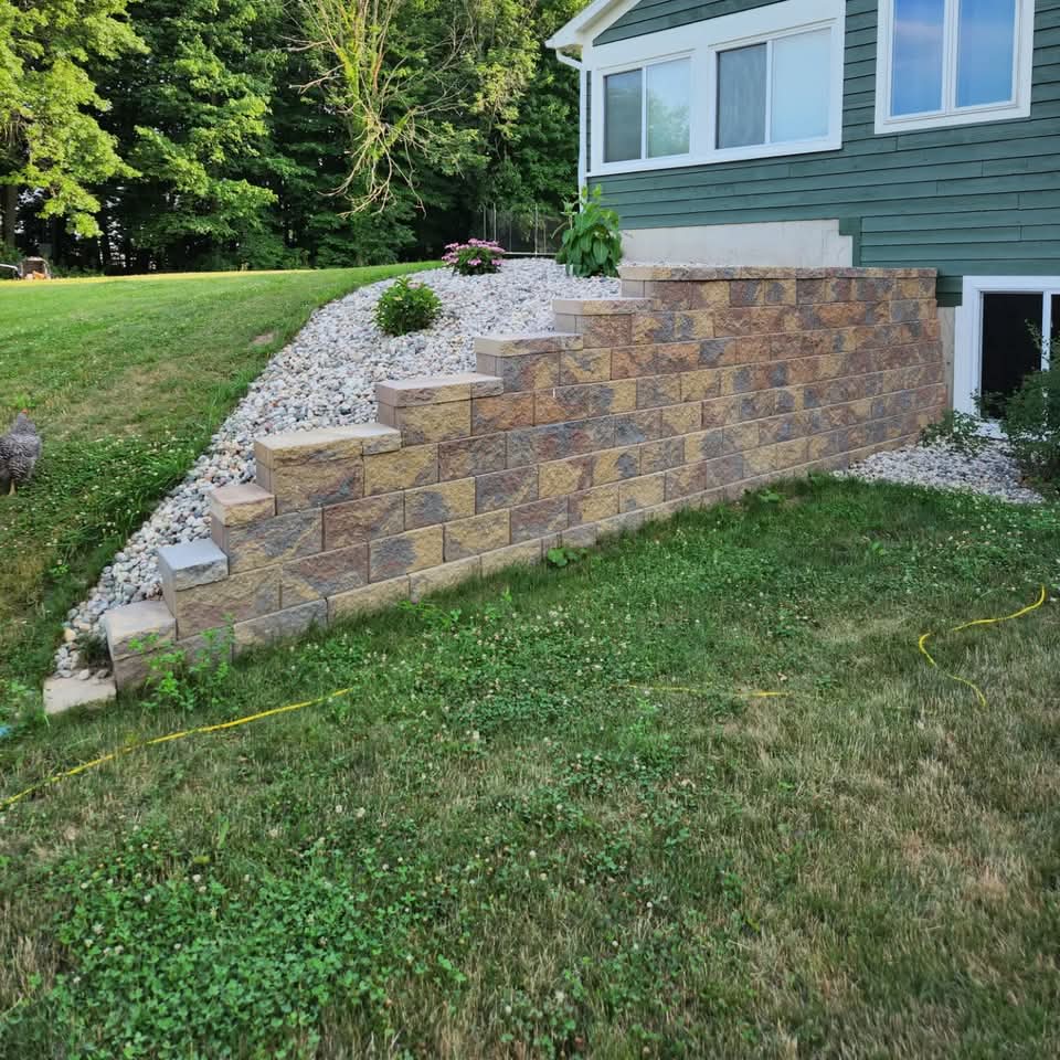 Front entry mulch beds with daffodils, planters, and a concrete walkway along a brick-front home