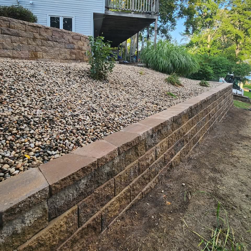 Curved front yard bed with dark mulch, ornamental shrubs, yellow spireas, a Japanese maple, and decorative boulders
