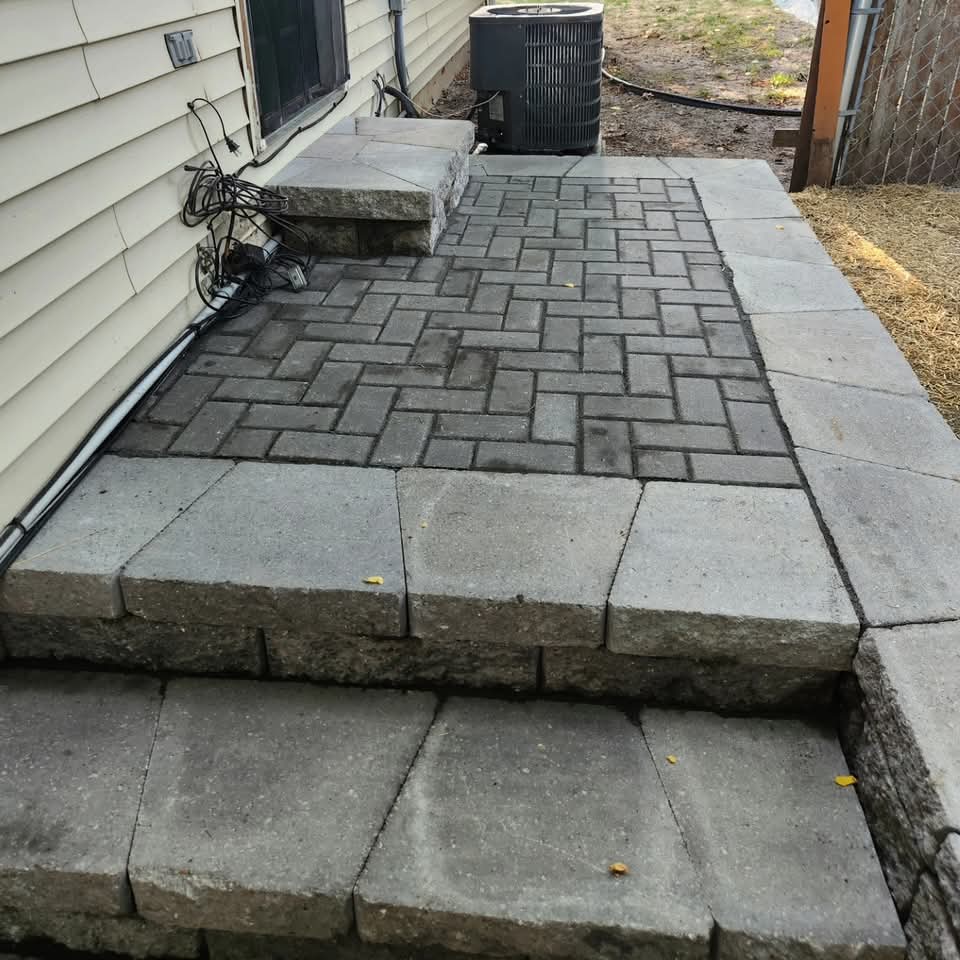 Raised paver landing with herringbone pattern, block steps, and retaining wall next to a sliding glass door