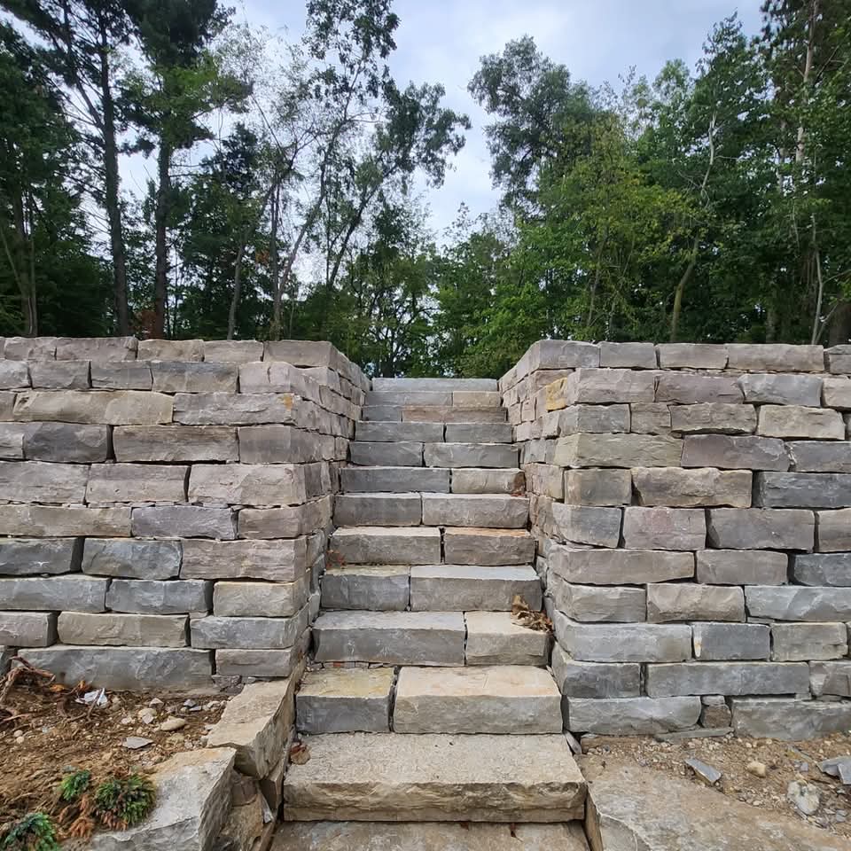 Natural stone staircase with rough-cut limestone steps and retaining walls flanking both sides looking uphill through trees