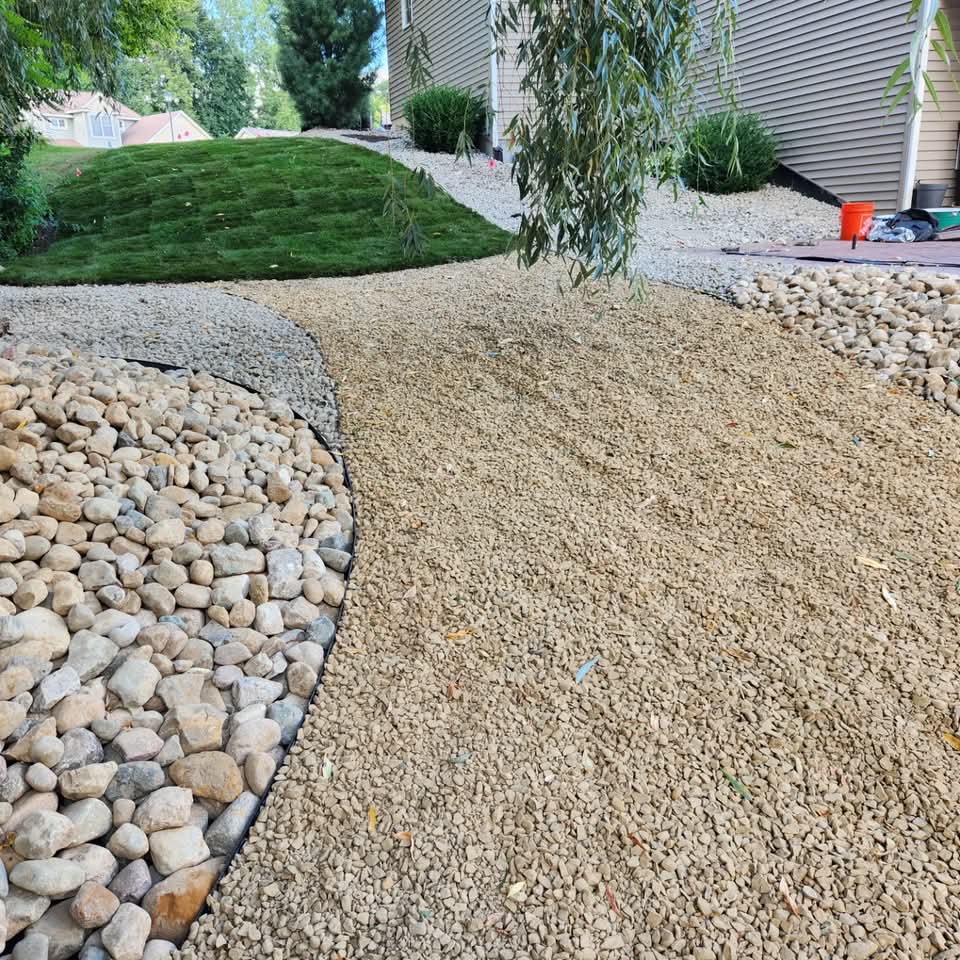 Subsurface drainage strip of pea gravel framed by river rock alongside a freshly sodded lawn
