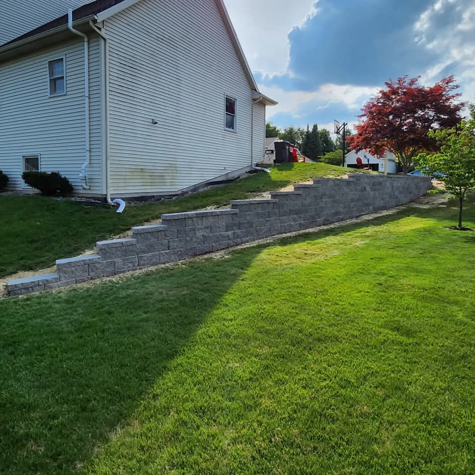 Green lawn fronting a gray block retaining wall on the side of a home