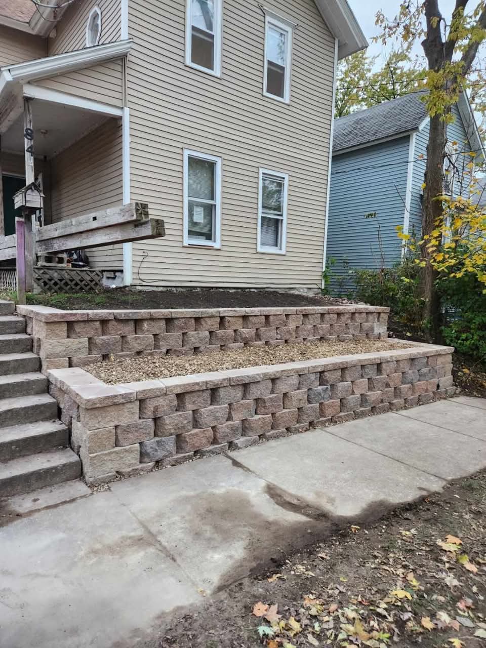 Two-tier block retaining wall with gravel planter and block steps leading up to the porch of a house