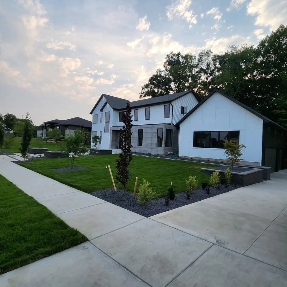 Side yard with dark block retaining walls, integrated block steps with light cap stones, gravel bed, paver patio below, and trimmed shrubs on the wall cap