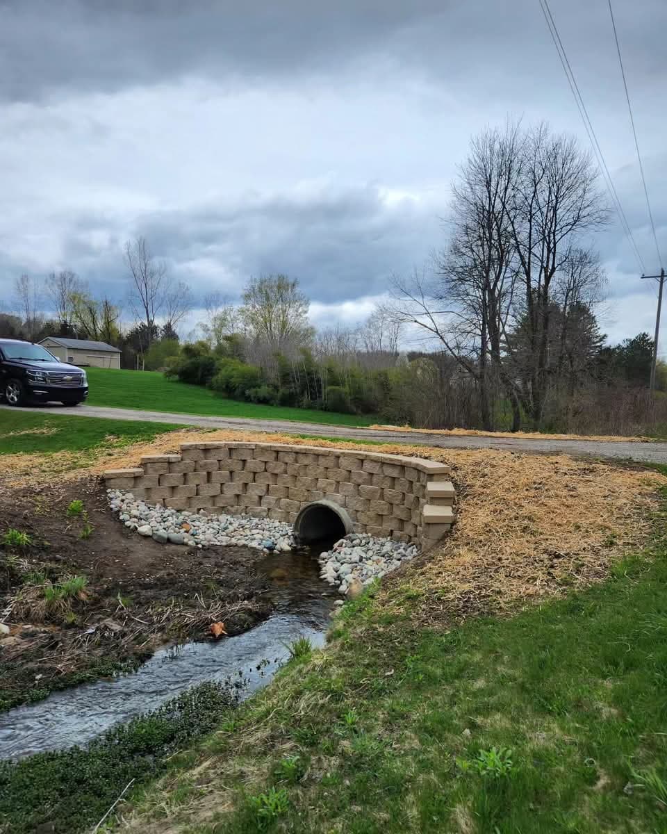Block retaining wall headwall around a culvert pipe with river rock riprap over a stream and straw erosion blanket
