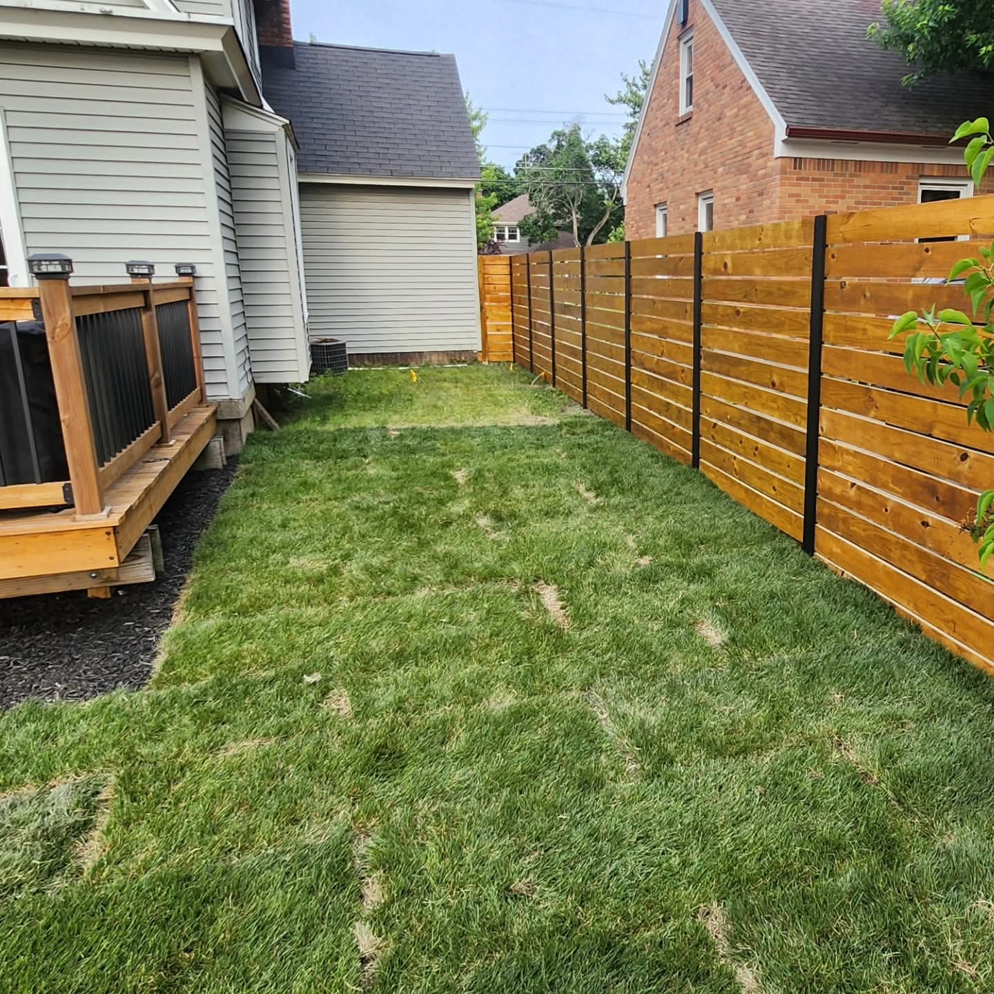Narrow strip of freshly laid sod between a home's siding and a new horizontal-board wood fence