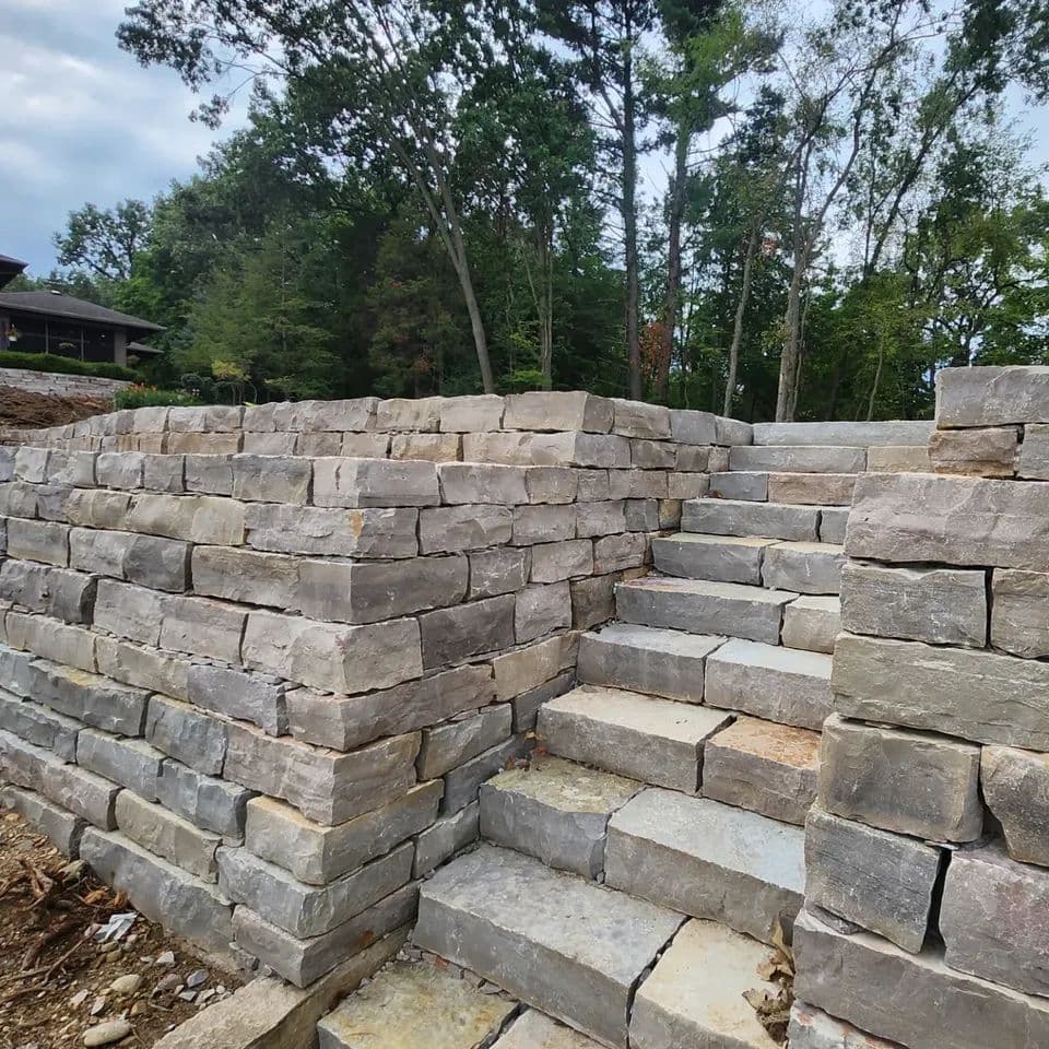 Rustic natural stone retaining wall with built-in staircase ascending a wooded slope